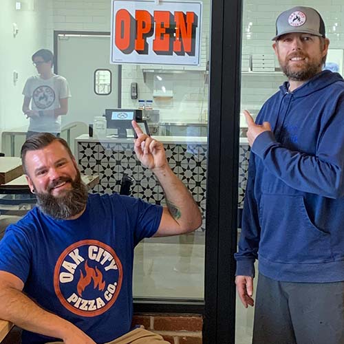 Owners Matt and Matt Pointing to Open Sign at Oak City Pizza