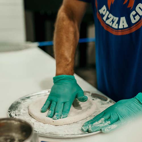 Oak City Pizza employee pressing down pizza dough
